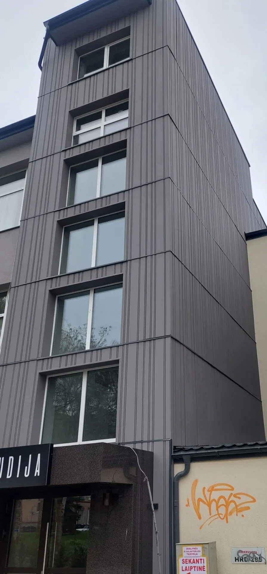 Komercinio pastato fasadas, apdailintas tamsiomis fasado plokštėmis